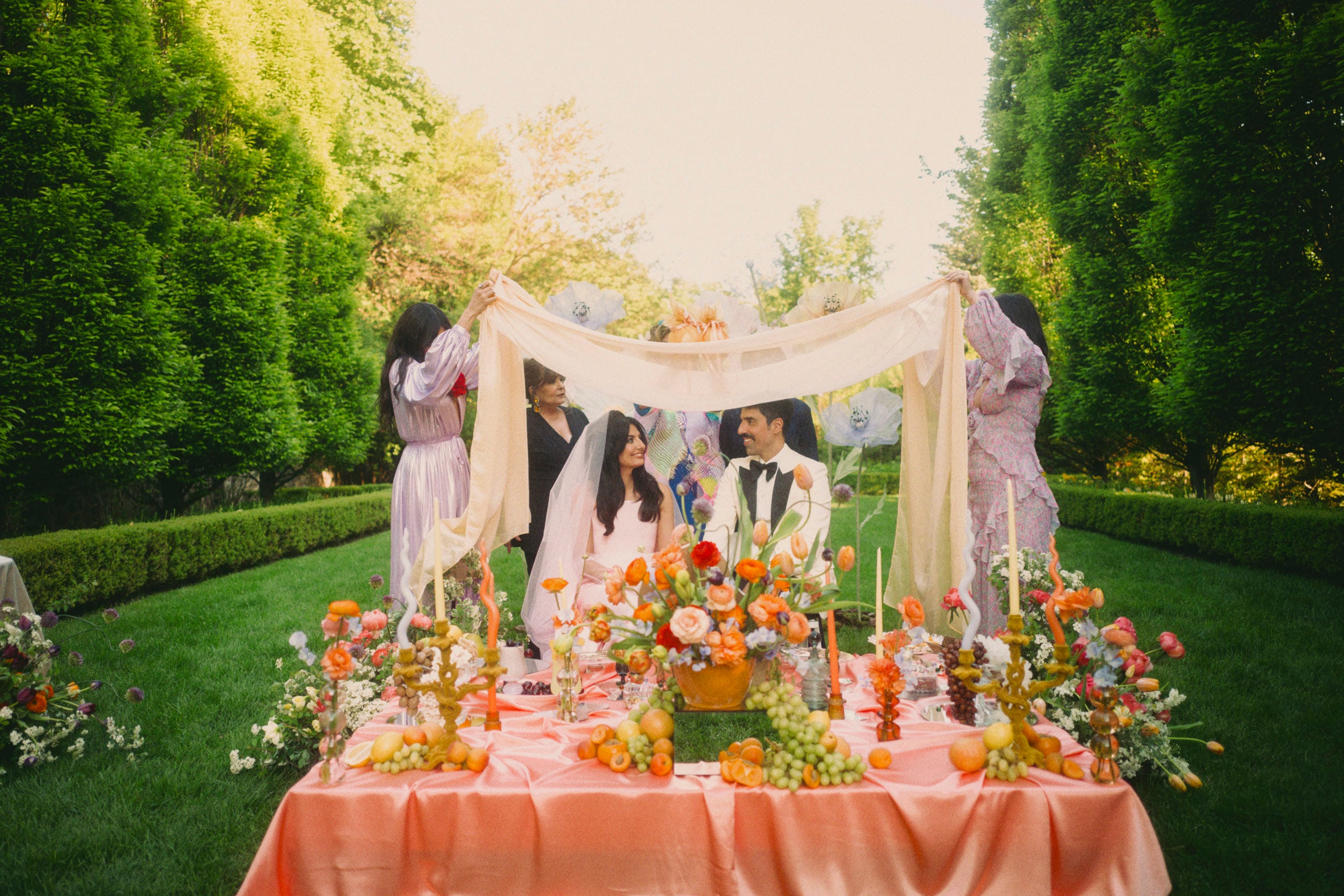 Roya and Mani stting underneath their Sofreh Aghd alter