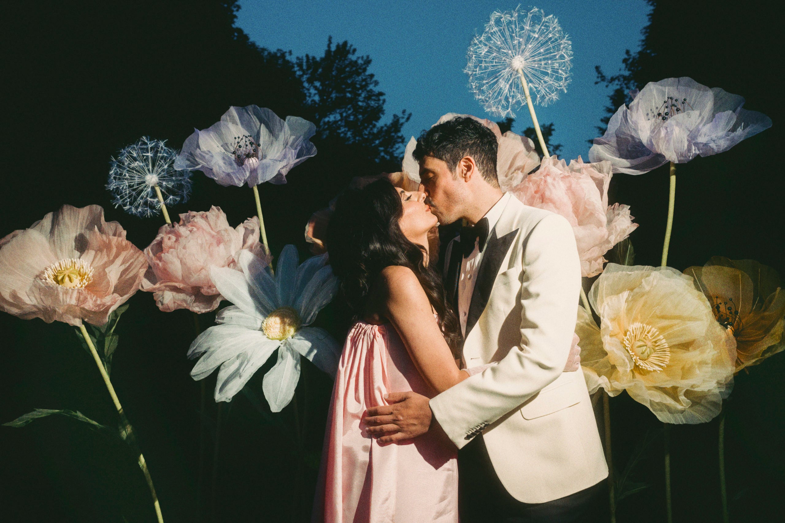 Roya and Mani kissing in front of a large flower arrangement
