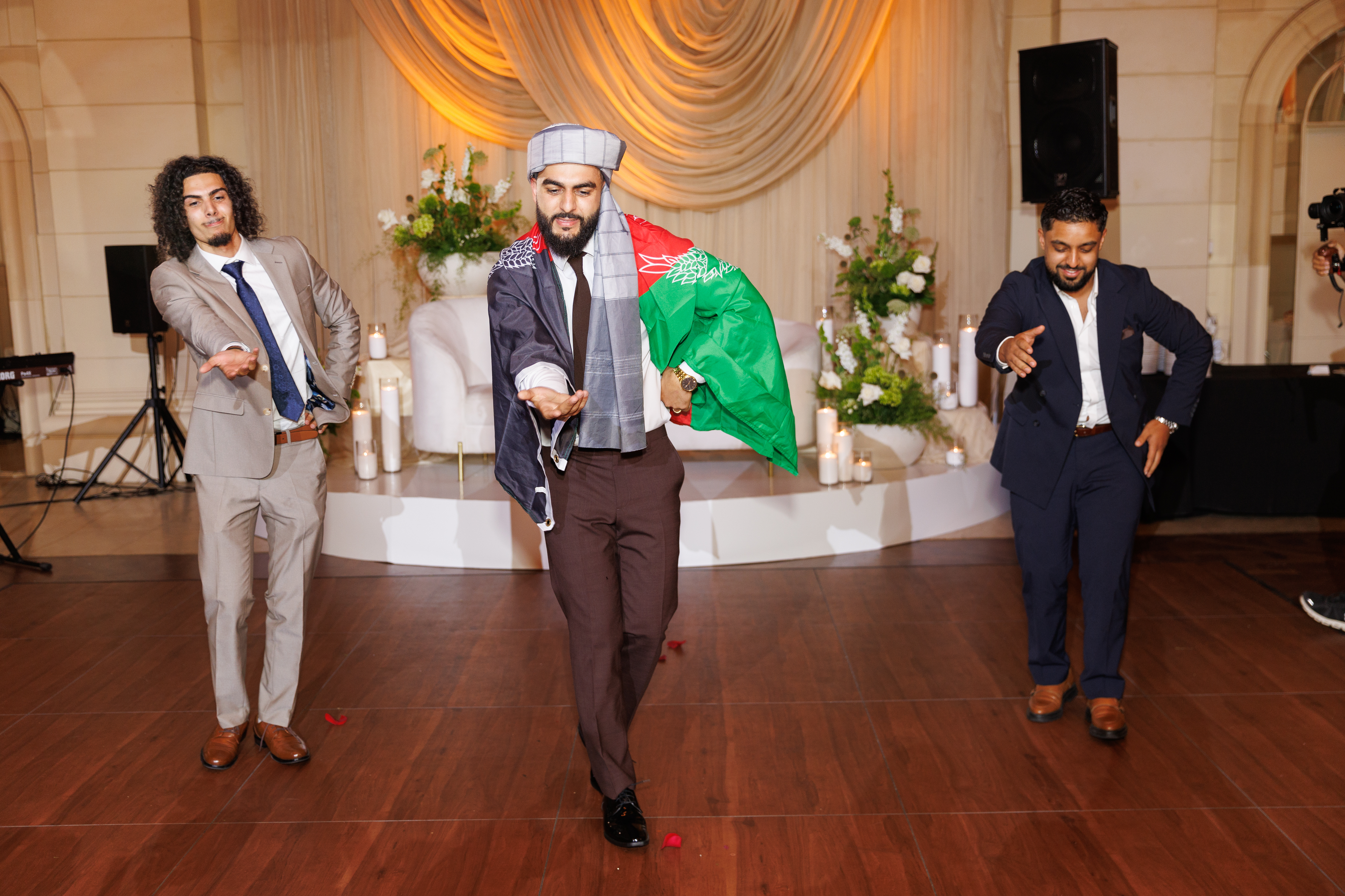 Harris dances a coordinated dance with two other men. He has a flag of Afghanistan draped over his shoulders.