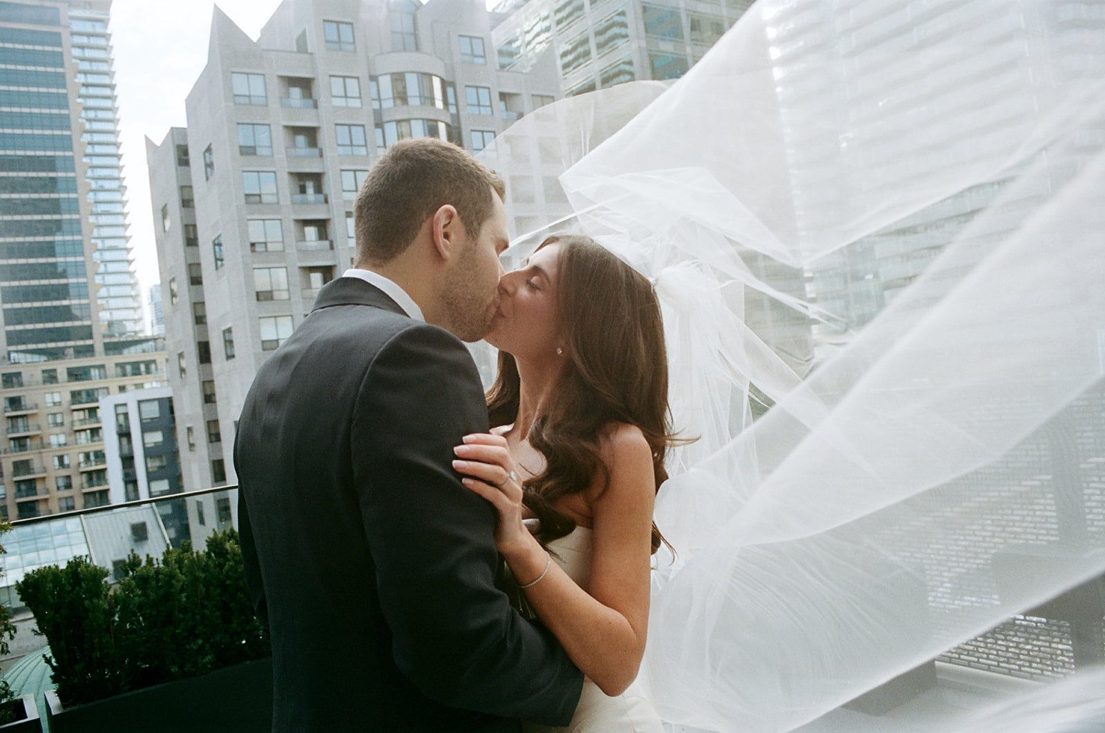 Bride and groom kiss while veil blows in the wind