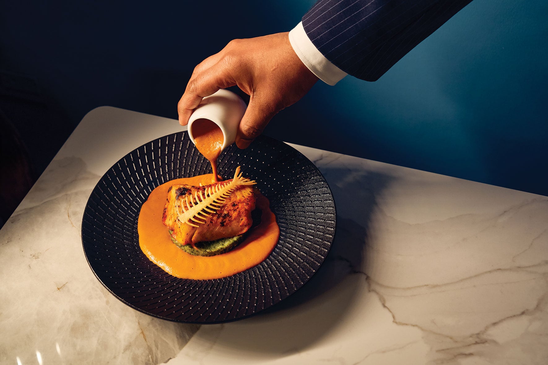 A server pours sauce over a fish dish at Aangan